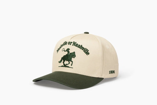 Front 3/4 view of a cream and dark green baseball cap with "Nashville or Nashville" text arcing over an embroidered cowboy on a horse logo, plus "1806" on the side.