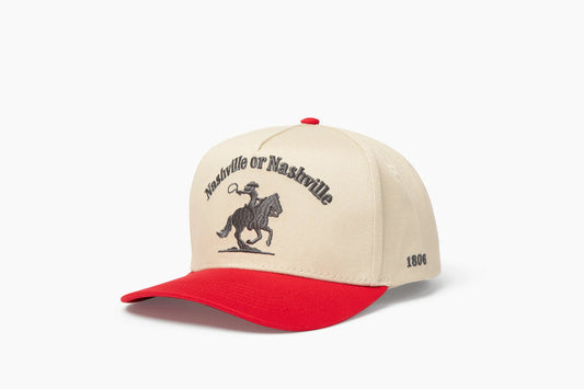 Front 3/4 view of a cream and red baseball cap with "Nashville or Nashville" text arcing over an embroidered cowboy on a horse logo, plus "1806" on the side.