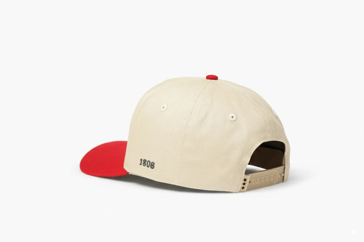Beige baseball cap with red brim, featuring "1806" embroidered on the back and three black star details on the adjustable strap. Back view.
