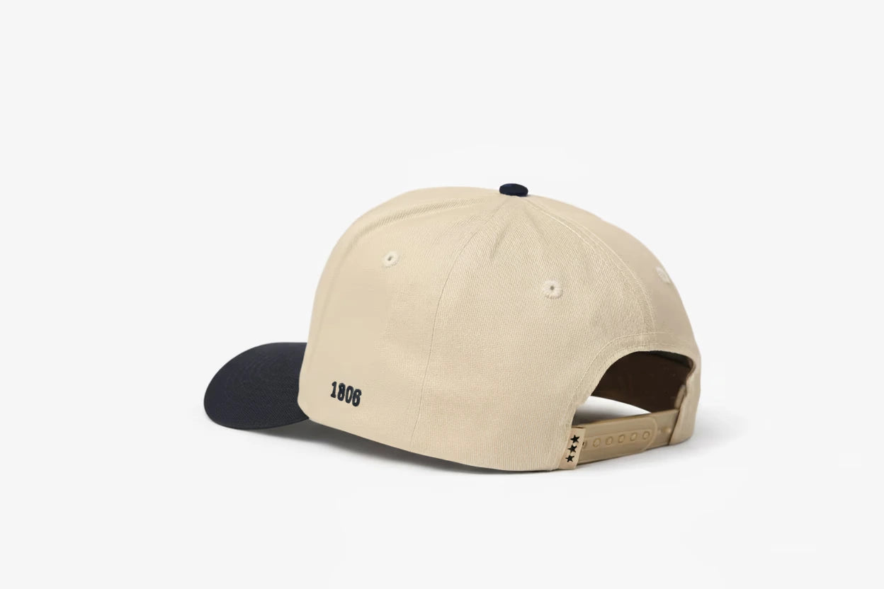 Beige baseball cap with dark blue brim, featuring "1806" embroidered on the back and three black star details on the adjustable strap. Back view.