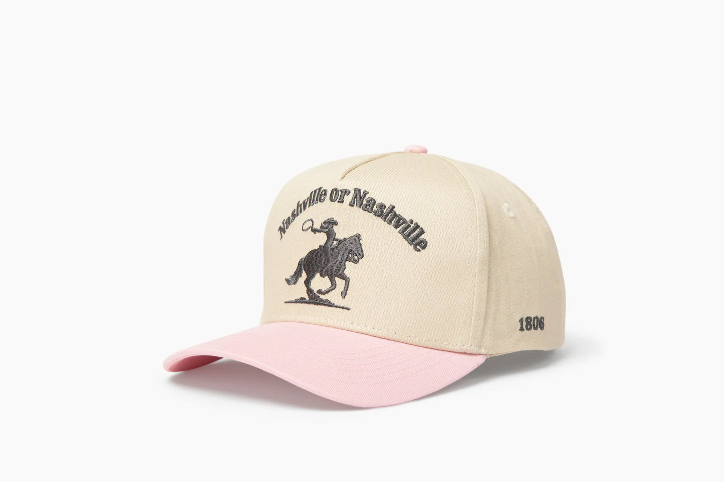 Front 3/4 view of a cream and pink baseball cap with "Nashville or Nashville" text arcing over an embroidered cowboy on a horse logo, plus "1806" on the side.