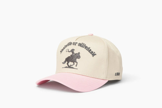 Front 3/4 view of a cream and pink baseball cap with "Nashville or Nashville" text arcing over an embroidered cowboy on a horse logo, plus "1806" on the side.