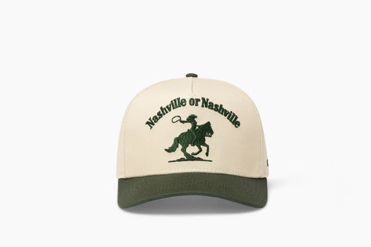 Front view of a beige baseball cap with a prominent dark green brim, showcasing "Nashville or Nashville" embroidered above a cowgirl riding a horse graphic.