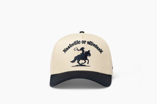 Front view of a beige baseball cap with a prominent dark blue brim, showcasing "Nashville or Nashville" embroidered above a cowgirl riding a horse graphic.